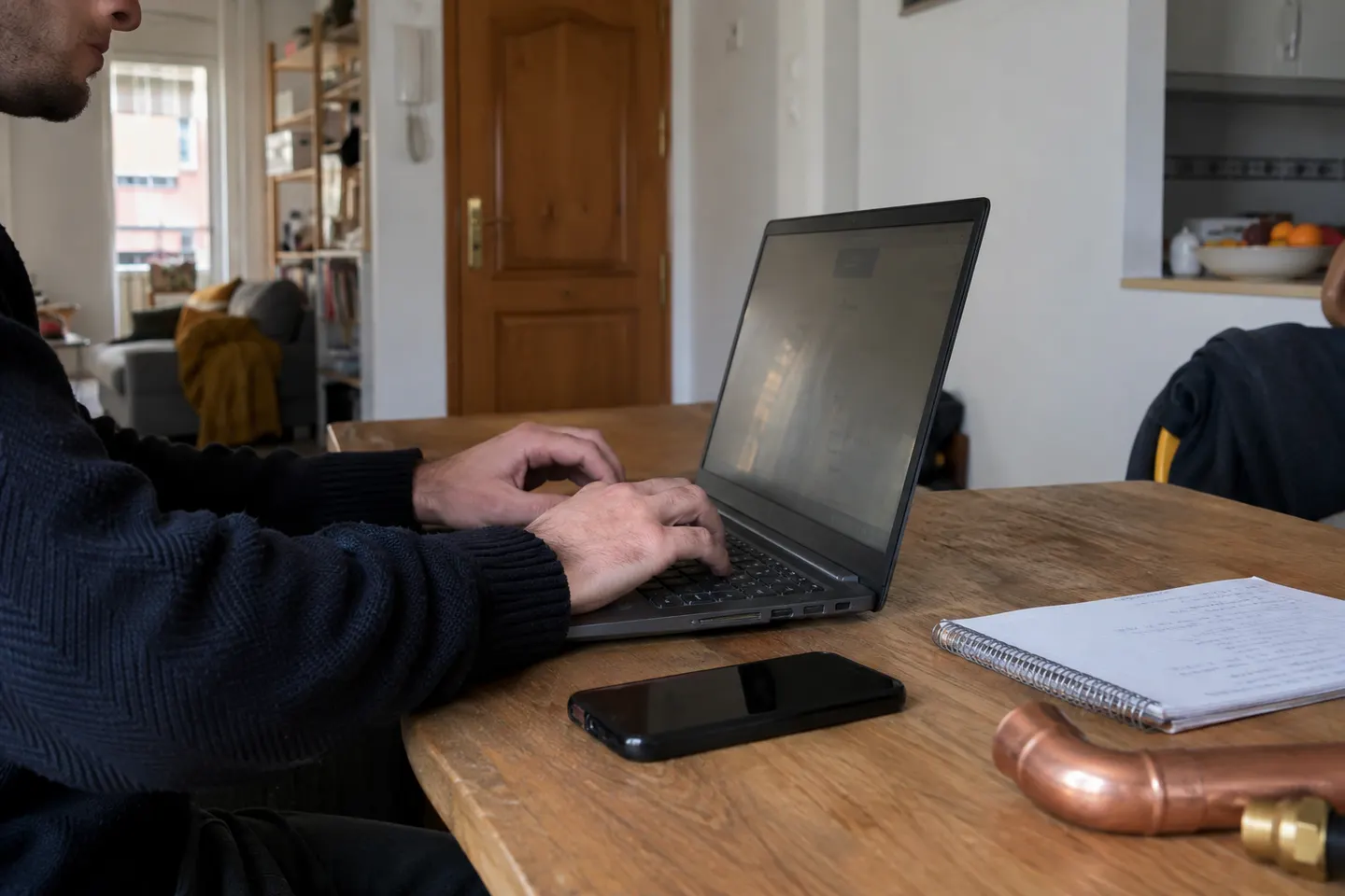 Manos escribiendo en un portátil junto a un cuaderno de consulta